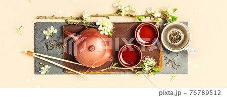 Asian Tea set on stone slate board, ceramic teapot, cups, dried tea and spring branches 76789512