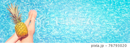 Pineapple in hand on legs and swimming pool background. 76793020