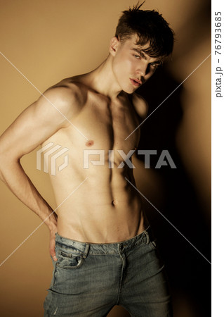 Muscle strong beautiful stripped male model in denim blue jeans on beige isolated font background 76793685