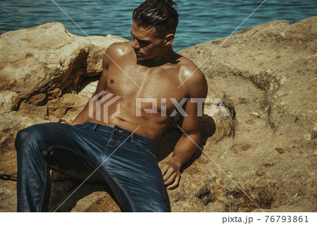 Strong face sexy sport male model in wet blue jeans in sea water on stones background 76793861