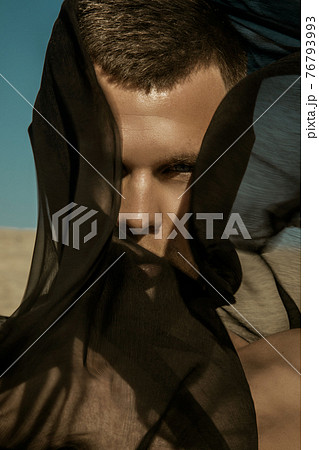 Guy with black scarf and wind on sky background in dessert Guy with black scarf and wind on sky background in dessert 76793993