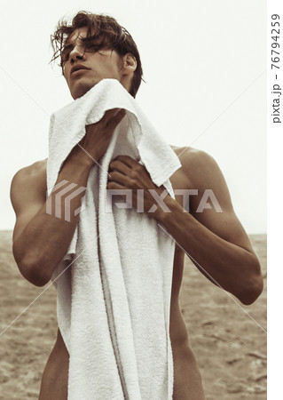Sexy beautiful striped male model with white towel on the nature background with sand and sky on the beach on the sunset Sexy beautiful striped male model with white towel on the nature background with sand and sky on the beach on the sunset 76794259
