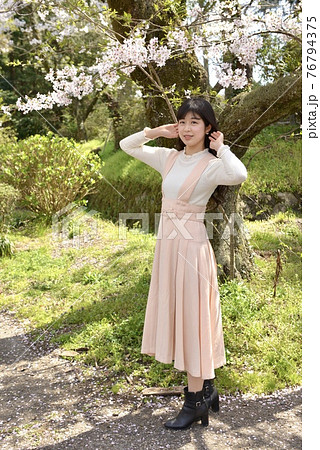 サクラ咲く公園でポーズをとる若くスリムな女性 76794375