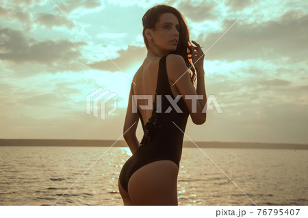 Stunning beautiful dark hair girl stripped in swimsuit on the sunset at he beach Stunning beautiful dark hair girl stripped in swimsuit on the sunset at he beach 76795407