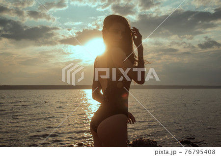 Stunning beautiful dark hair girl stripped in swimsuit on the sunset at he beach Stunning beautiful dark hair girl stripped in swimsuit on the sunset at he beach 76795408