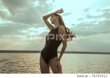 Stunning beautiful dark hair girl stripped in swimsuit on the sunset at he beach Stunning beautiful dark hair girl stripped in swimsuit on the sunset at he beach 76795413