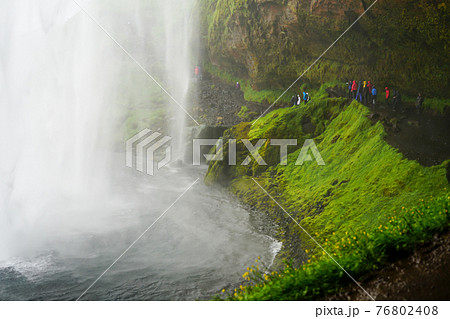 アイスランドのセリャラントスフォスの滝の裏側を歩く観光客の写真素材