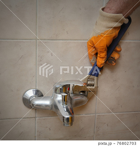 Plumber fixing old tap in a bathroom using adjustable wrench 76802703