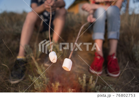 two children, a boy and a girl are holding on their sticks white marshmallows over a bonfire, concept, hike, camping holiday, sweet supper, close-up of shooting 76802753
