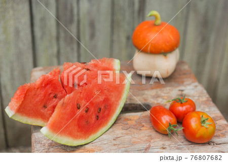 two slices of a ripe watermelon on an old wooden board, next to three red tomatoes and a mushroom in the form of a mushroom, the concept of autumn, selective focusing two slices of a ripe watermelon on an old wooden board, next to three red tomatoes and a mushroom in the form of a mushroom, the concept of autumn, selective focusing 76807682