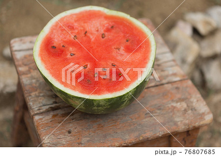 a ripe watermelon is cut and half a red watermelon lies on an old wooden stool, a rustic style, selective focusing a ripe watermelon is cut and half a red watermelon lies on an old wooden stool, a rustic style, selective focusing 76807685