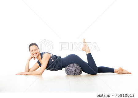 Restorative yoga with a bolster. Young sporty female yoga instructor in bright white yoga studio, lying on bolster cushion, stretching, smilling, showing love and passion for restorative yoga Restorative yoga with a bolster. Young sporty female yoga instructor in bright white yoga studio, lying on bolster cushion, stretching, smilling, showing love and passion for restorative yoga 76810013