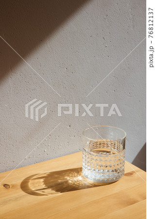 A glass with clean clear water and sharp shadows stands on a wood table on gray wall background A glass with clean clear water and sharp shadows stands on a wood table on gray wall background 76812137