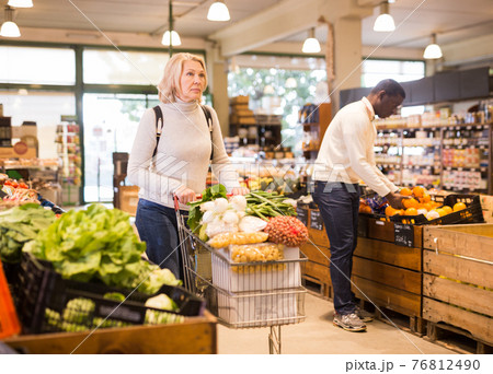 Woman carrying purchases in trolley cart 76812490