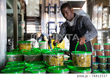 Man arranging plastic buckets with pickled olives 76812537