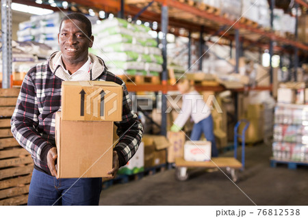 Smiling man carrying boxes in warehouse 76812538
