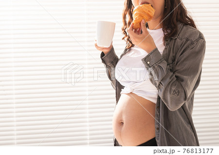 Healthy beautiful pregnant woman drinking tea and eating croissant during lunch. Concept of high-calorie nutrition while waiting for birth of baby. Copy space. Healthy beautiful pregnant woman drinking tea and eating croissant during lunch. Concept of high-calorie nutrition while waiting for birth of baby. Copy space. 76813177