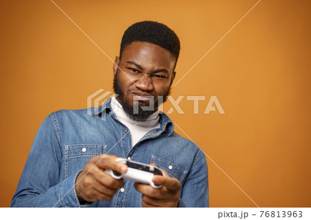 Young african american man holding joystick playing video games, yellow background 76813963