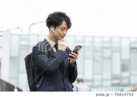 スマホの画面を見るヘッドホンをした30代前半の男性 76814703