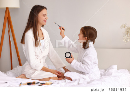 Happy mother applying makeup on face of daughter 76814935