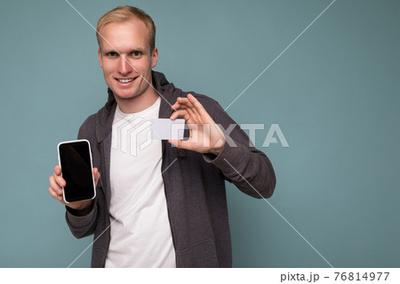 Handsome smiling blonde man wearing grey sweater and white t-shirt isolated over blue background Handsome smiling blonde man wearing grey sweater and white t-shirt isolated over blue background 76814977