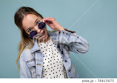 Shot of pretty positive joyful young blonde woman wearing blue jean jacket and stylish sunglasses 76815675