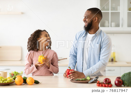 Cheerful african father and daughter cooking healthy salad 76817947
