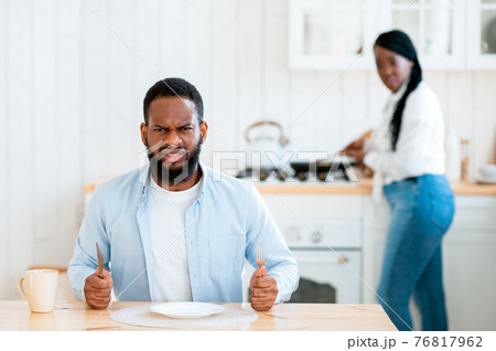 Starving Angry Black Man Waiting For Food At Table In Kitchen Starving Angry Black Man Waiting For Food At Table In Kitchen 76817962