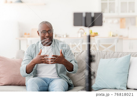 Middle-aged black male blogger broadcasting from home, gesturing and looking at smartphone Middle-aged black male blogger broadcasting from home, gesturing and looking at smartphone 76818021