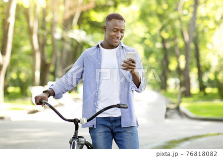 Cool African American guy with modern bike sending message on cellphone at park Cool African American guy with modern bike sending message on cellphone at park 76818082