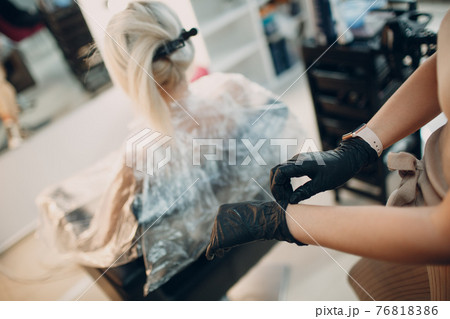Young woman hairdresser puts on gloves and preparing dying hair at beauty salon. Professional hair roots coloring 76818386