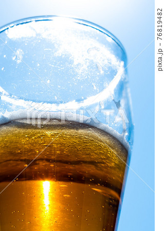Light beer in a glass goblet on a background of blue sky. Beer foam on the walls of a glass in the sunlight. Light beer in a glass goblet on a background of blue sky. Beer foam on the walls of a glass in the sunlight. 76819482