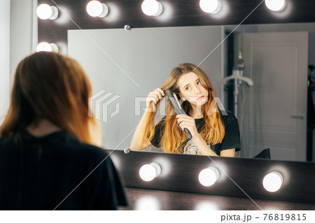 Young cute girl teen using a hair straightener on her wavy red hair 76819815