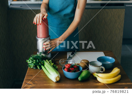 Close-up of a woman in the kitchen makes a pink smoothie of fruits and berries for breakfast. 76819821