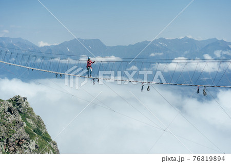 A person walks on a suspended rope bridge in the clouds. A person walks on a suspended rope bridge in the clouds. 76819894