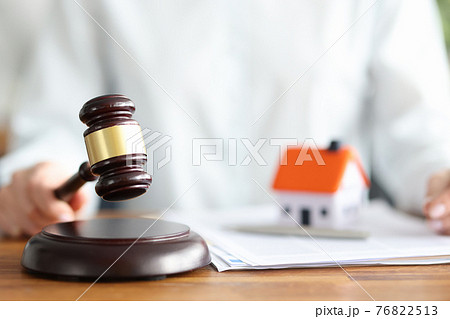 Judge holds judge wooden gavel against background of house and documents 76822513