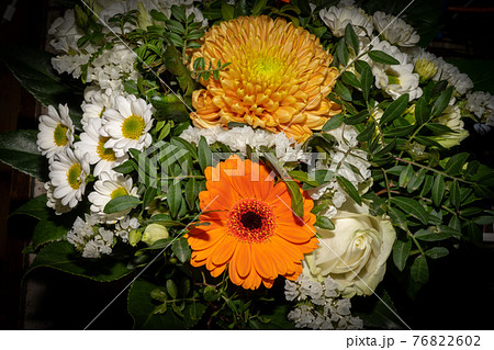 A close-up picture of a bouquet of funeral flowers. White, yellow and orange flowers with green leaves A close-up picture of a bouquet of funeral flowers. White, yellow and orange flowers with green leaves 76822602