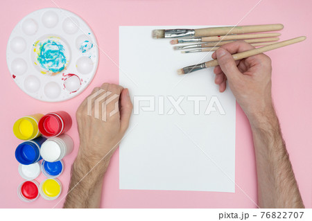 The artist paints with acrylics. Holds a brush in his hand. Mockup flat lay. Artist's hand over a blank canvas. The artist paints with acrylics. Holds a brush in his hand. Mockup flat lay. Artist's hand over a blank canvas. 76822707