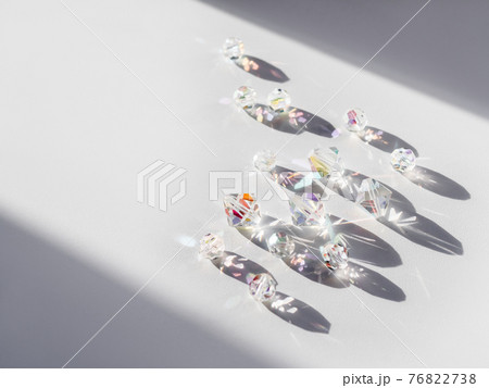 Sparkling glass beads on hard sunlight. Geometrical shadow and rainbow sun beams and reflections on transparent spangles. Jewellery on white background. Sparkling glass beads on hard sunlight. Geometrical shadow and rainbow sun beams and reflections on transparent spangles. Jewellery on white background. 76822738