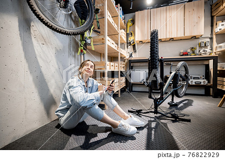 Handywoman with phone and bicycle in the workshop at home 76822929