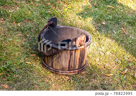 wooden bucket old and weathered with a handle stands on the grass close-up 76822995