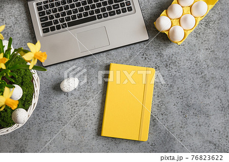Easter workspace with yellow notebook, flowers and laptop for planning holidays and shopping. 76823622