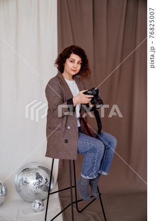 woman in jeans and checkered jacket on high chair in photo studio with camera woman in jeans and checkered jacket on high chair in photo studio with camera 76825007