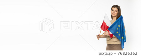 Young girl with the flag of the European Union and Poland. The student is holding two flags in her hand. Woman with flags on white background. Panoramic frame. Young girl with the flag of the European Union and Poland. The student is holding two flags in her hand. Woman with flags on white background. Panoramic frame. 76826362