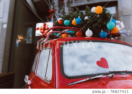 Red retro car with a Christmas tree fir tied to the roof. Red retro car with a Christmas tree fir tied to the roof. 76827421