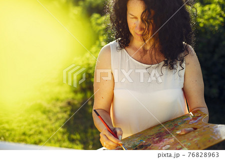 Beautiful adult woman drawing in a summer field Beautiful adult woman drawing in a summer field 76828963