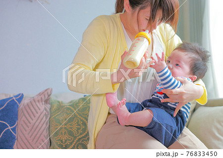 手を挙げて早くミルクをちょうだいとせがむ男の子と哺乳瓶を持つ母親の写真素材