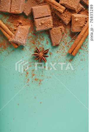 Dark chocolate slices with cinnamon and spices on a pastel green background. 76835289