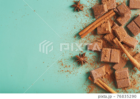 Dark chocolate slices with cinnamon and spices on a pastel green background. 76835290