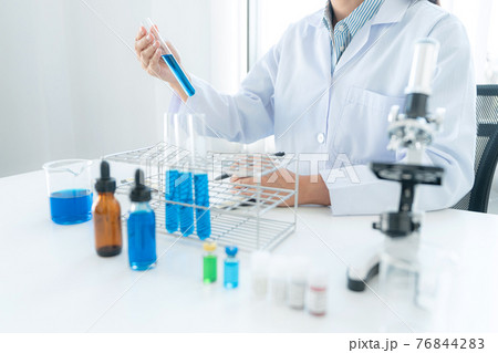 Scientist woman holding test tube in her hands and writing down result report on notebook while working 76844283